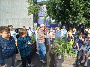 Az előadóterem épülete előtt, a szabadban, a résztvevők karéjában álló madarász a kezében tartott rigót készül elengedni.